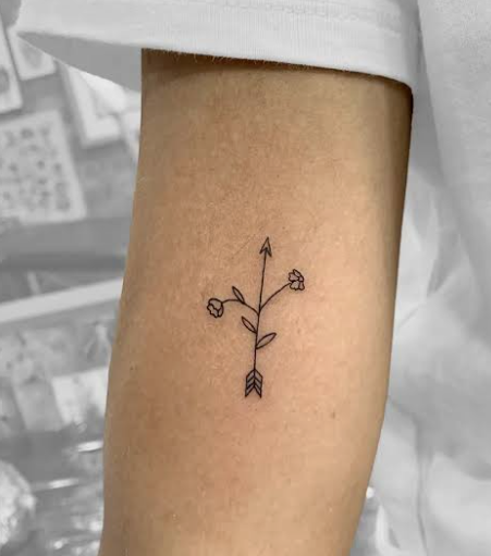 Minimalist fine line tattoo reference with a tiny flower and arrow on an arm